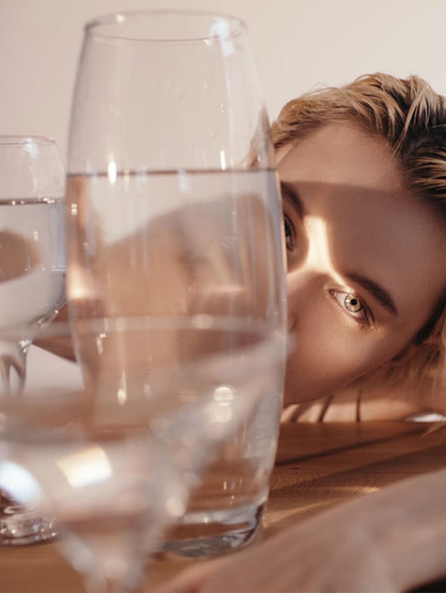 women leans agaianst a wooden table covered in water glasses