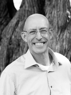 Michael Pollan in black and white stands infront of a tree smiling