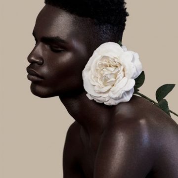 a black man infront of a nude background poses with a flower
