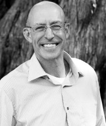 micheal pollan stands infront of a tree wearing a shirt and smiling at the camera in black and white