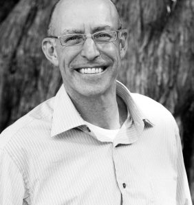 micheal pollan stands infront of a tree wearing a shirt and smiling at the camera in black and white