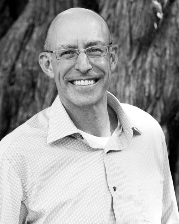 micheal pollan stands infront of a tree wearing a shirt and smiling at the camera in black and white