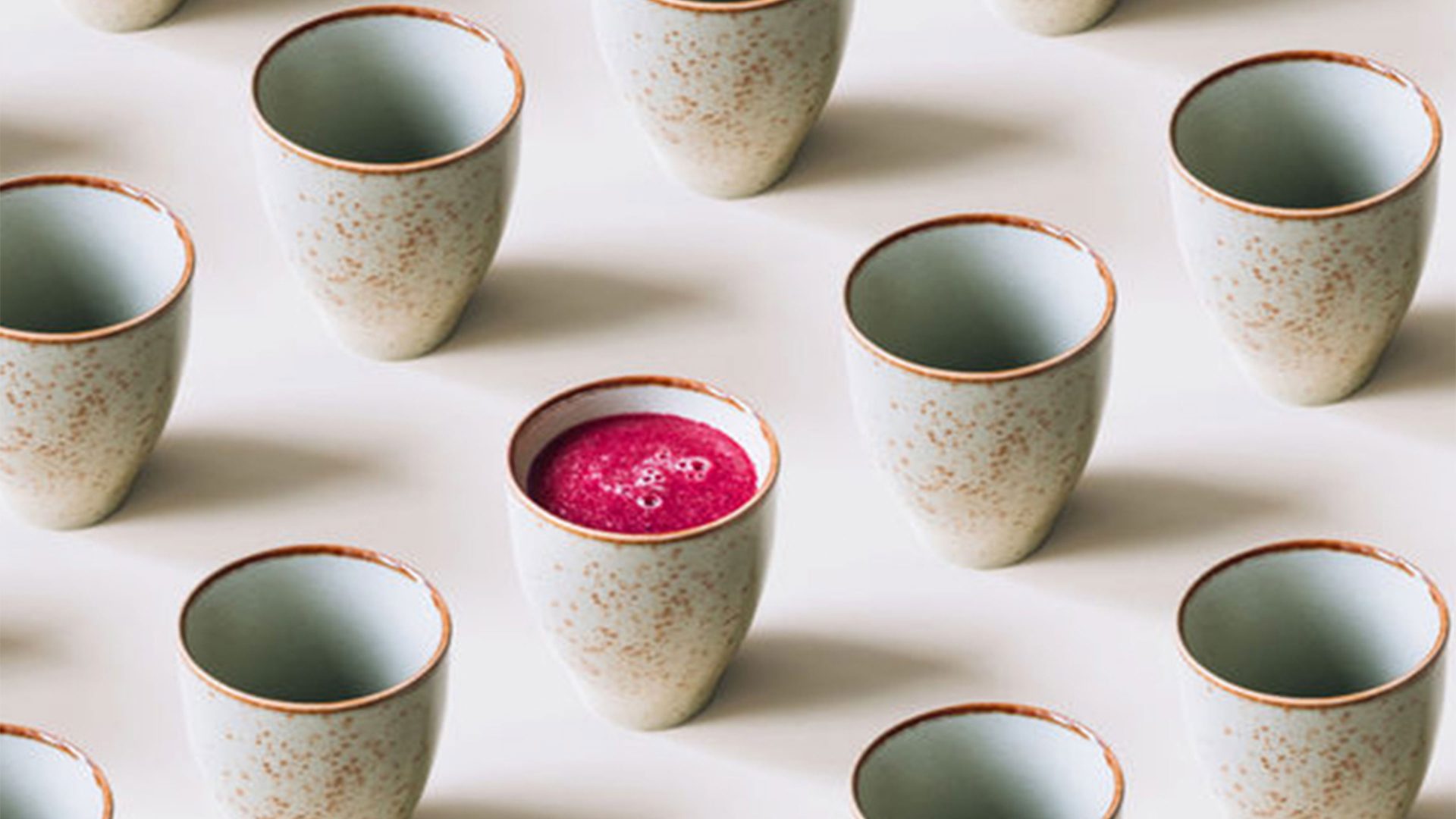 A row of ceramic Japanese inspired mugs with one mug containing pink juice