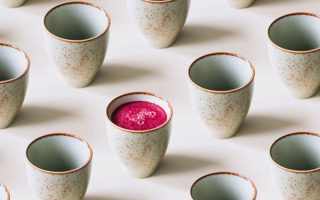 A row of ceramic Japanese inspired mugs with one mug containing pink juice