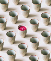A row of Japanese inspired ceramic mugs with one mug containing pink juice