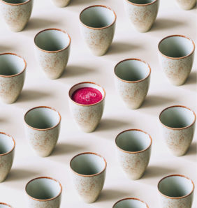A row of Japanese inspired ceramic mugs with one mug containing pink juice