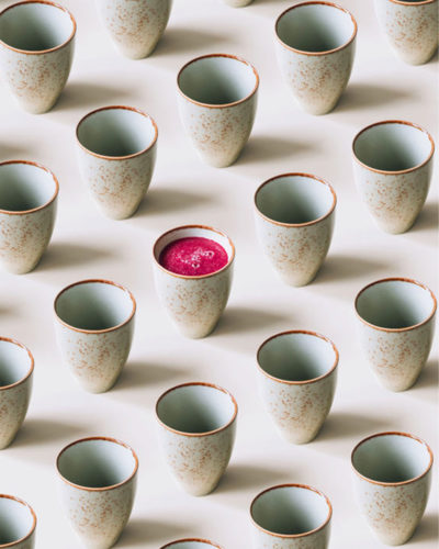 A row of Japanese inspired ceramic mugs with one mug containing pink juice