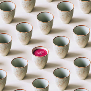 A row of Japanese inspired ceramic mugs with one mug containing pink juice