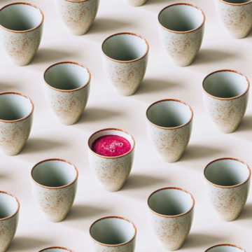A row of Japanese inspired ceramic mugs with one mug containing pink juice