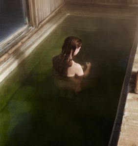 A red haired model sits in a green pool with her back turned
