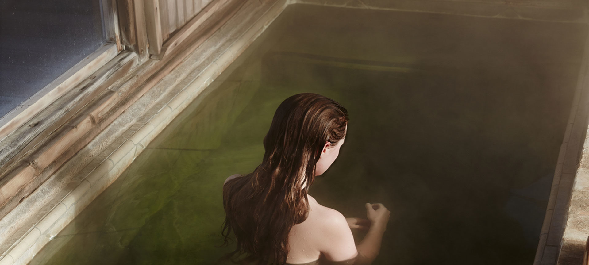 A red haired model sits in a green pool with her back turned