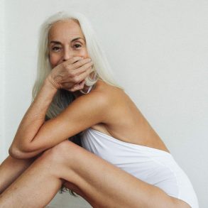 Model Yazemeenah Rossi sits with in a white bathing suit smiling at the camera