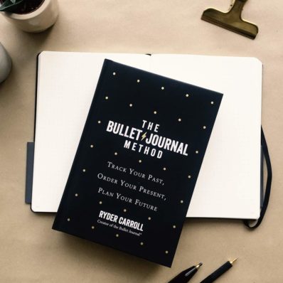 Bullet journal notebook and book on table with pens