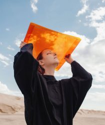 Girl holds up orange sheet against a blue sky