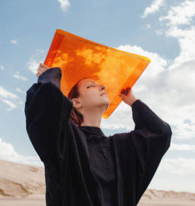 Girl holds up orange sheet against a blue sky