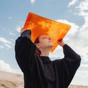 Girl holds up orange sheet against a blue sky