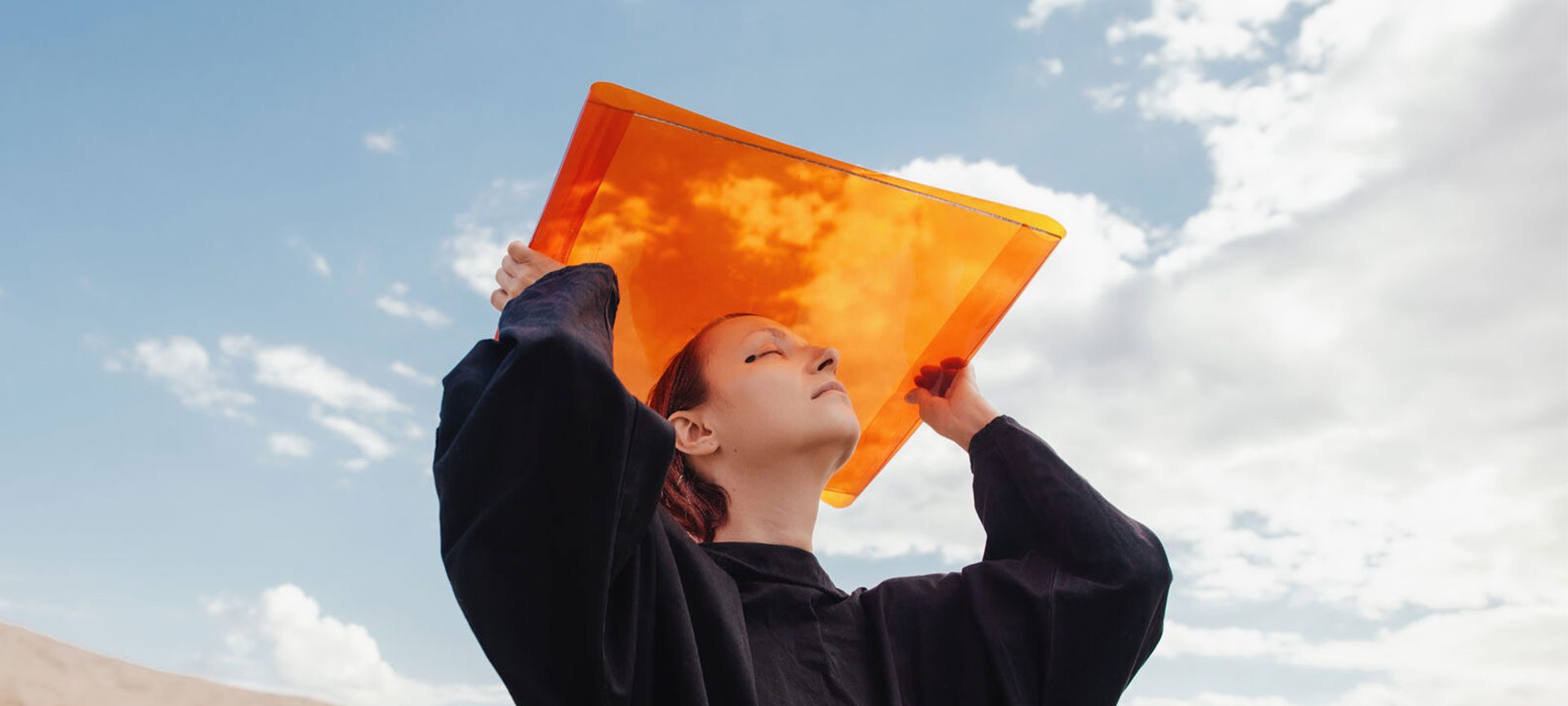 Girl holds up orange sheet against a blue sky