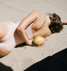 women lying on the sand with a mango