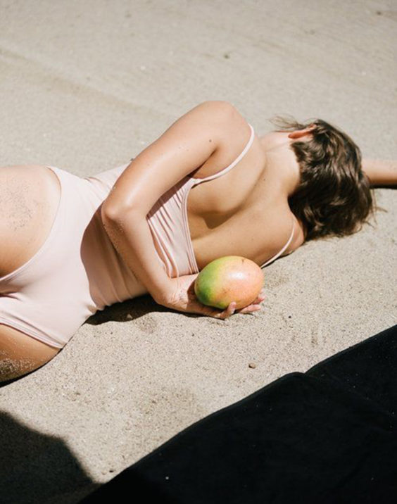women lying on the sand with a mango
