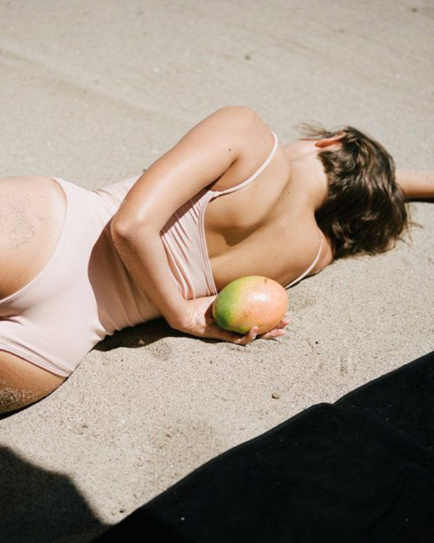 women lying on the sand with a mango