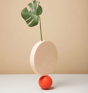a circular nude stone sits ontop of a small orange stone with a leaf