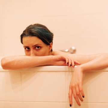 A female model sits in a pink bathtub looking out