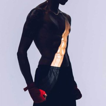 A male model in stands in boxing shorts and red gloves