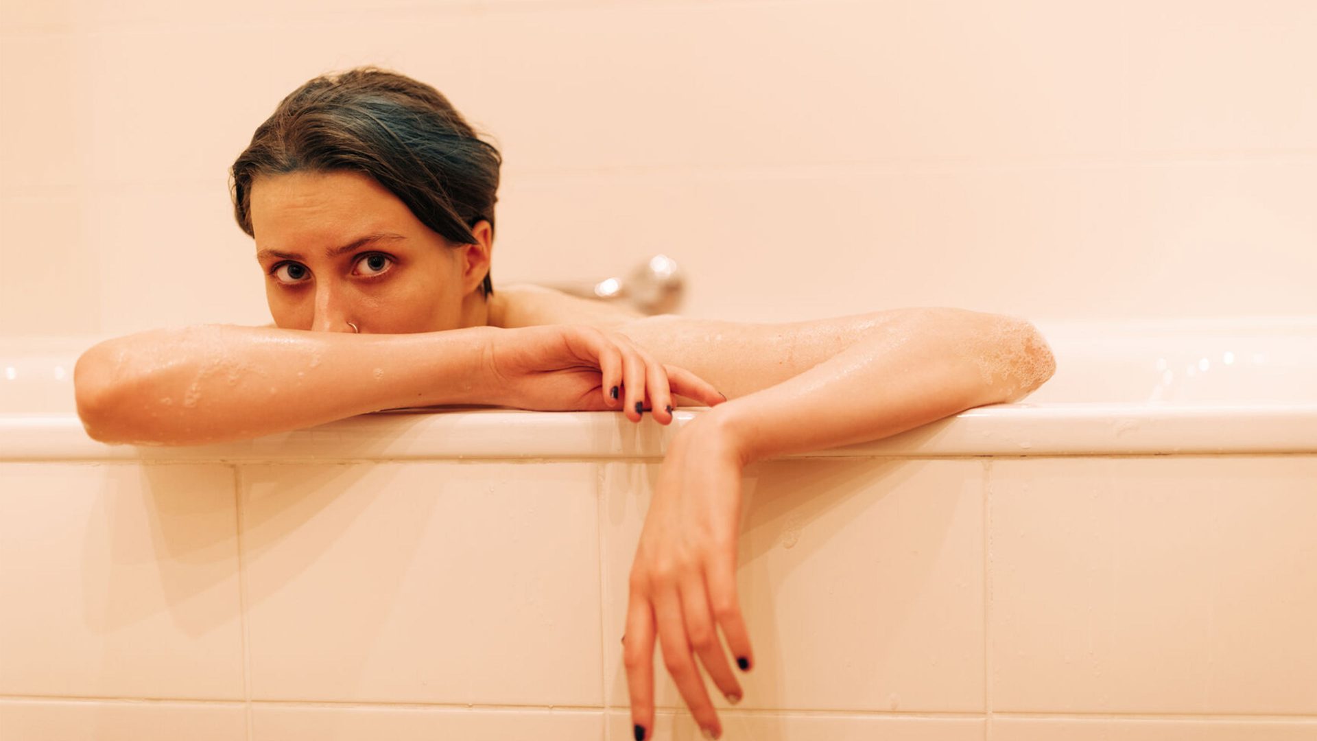 A female model sits in a pink bathtub looking out