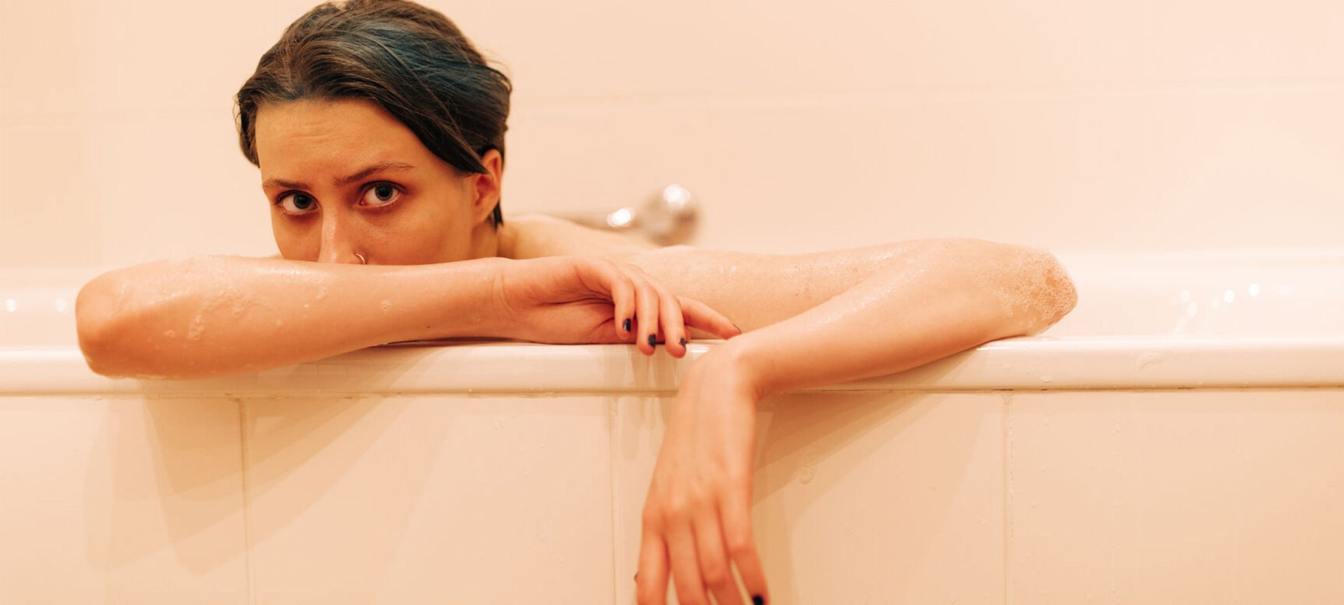 A female model sits in a pink bathtub looking out