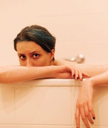 A female model sits in a pink bathtub looking out