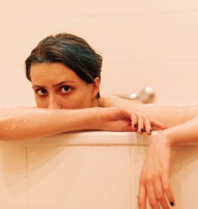 A female model sits in a pink bathtub looking out