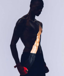 A male model in stands in boxing shorts and red gloves