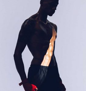 A male model in stands in boxing shorts and red gloves