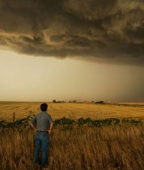 Storm chaser Tim Samaras looks across a field at dark storm clouds