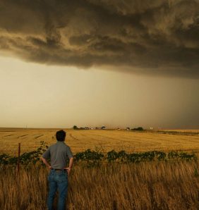 Storm chaser Tim Samaras looks across a field at dark storm clouds