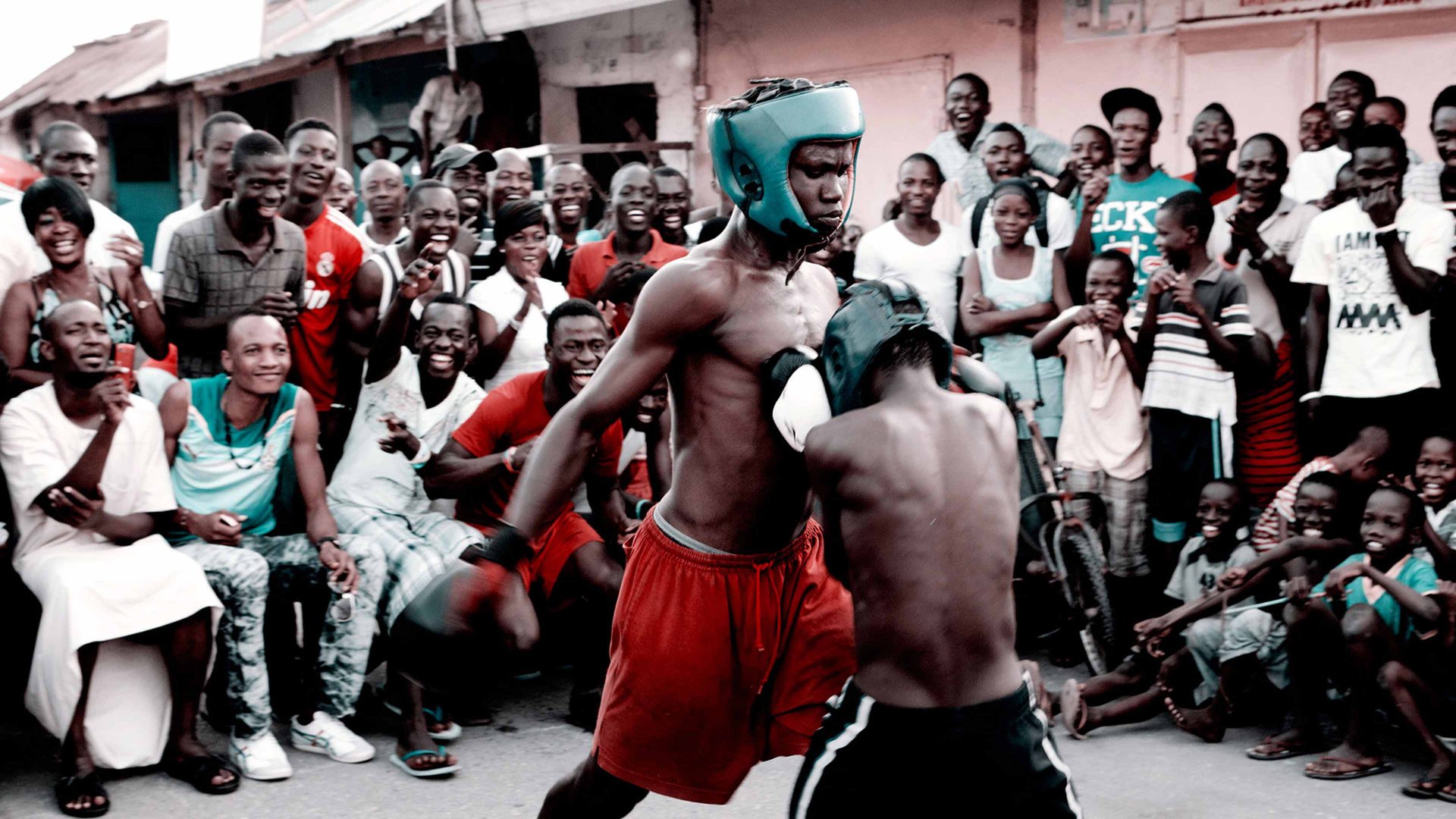 Two young Bukom boxers spar in a ring, cheered on by a crowd