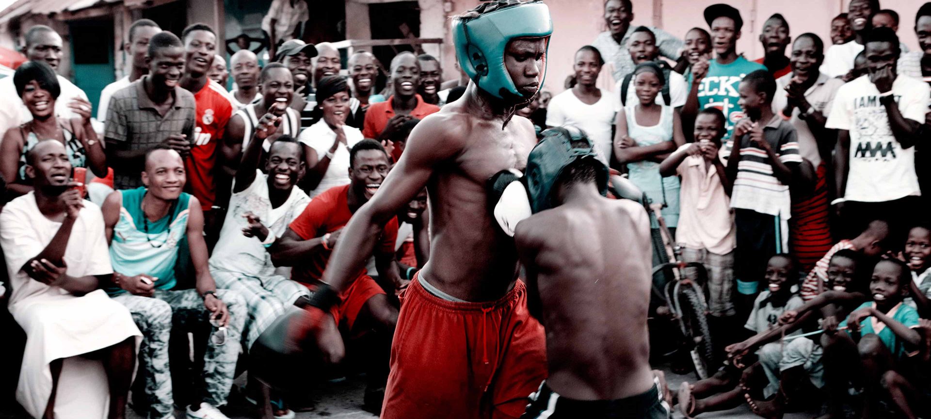Two young Bukom boxers spar in a ring, cheered on by a crowd