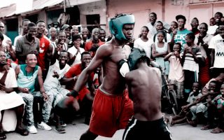 Two young Bukom boxers spar in a ring, cheered on by a crowd