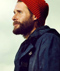 david de rothschild wears a red beanie and outdoor coat infront of a pale green background