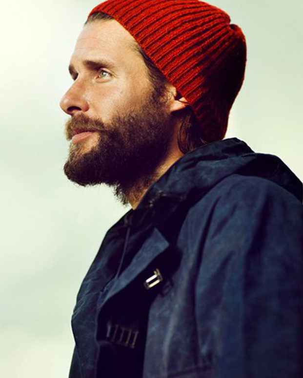 david de rothschild wears a red beanie and outdoor coat infront of a pale green background