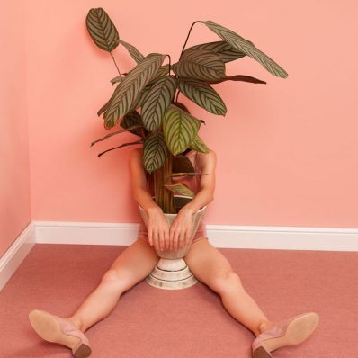 Female model sitting on the floor with a plant pot in pink room