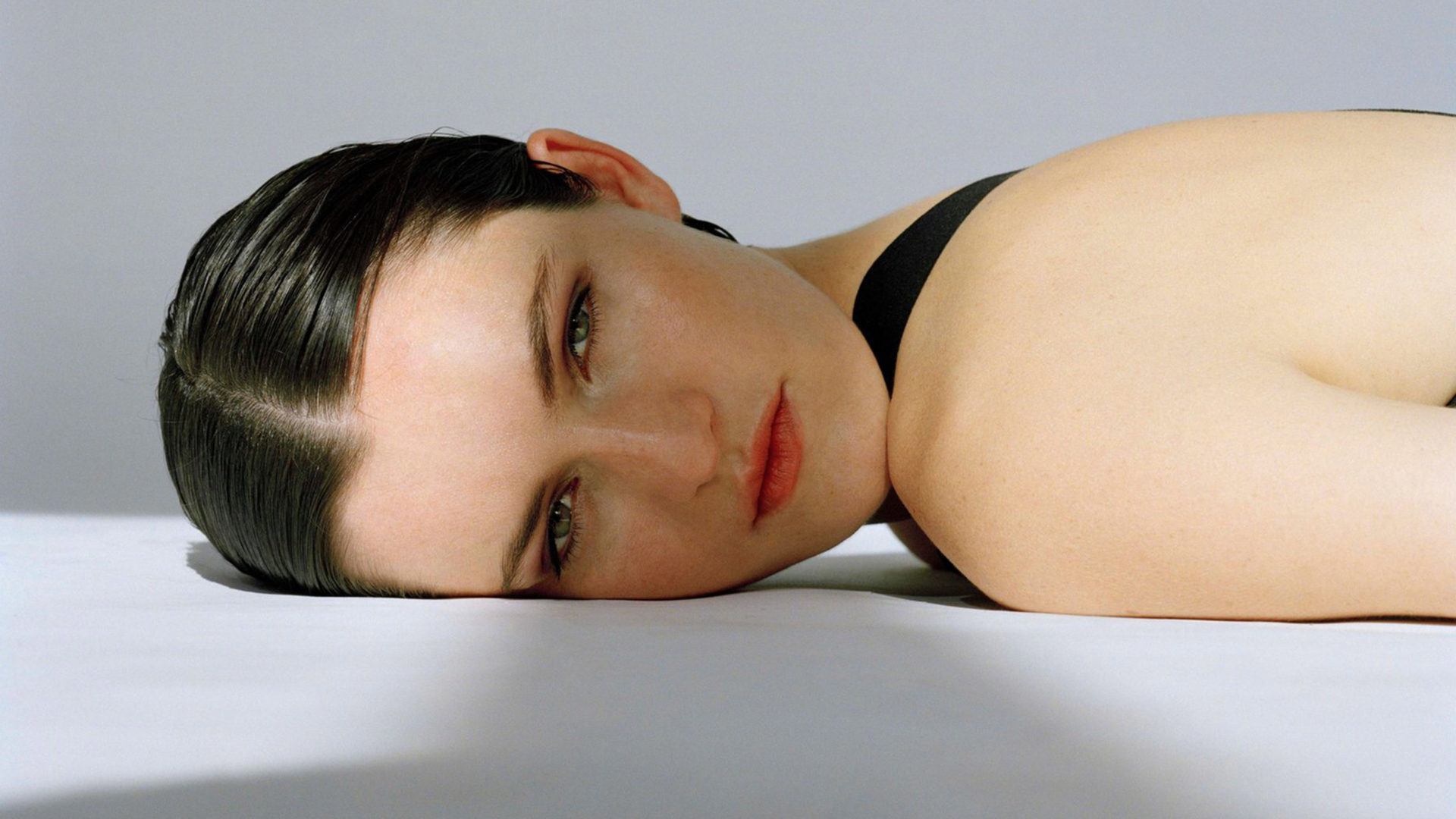 a woman lies looking at the camera on a grey floor