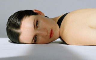 a woman lies looking at the camera on a grey floor