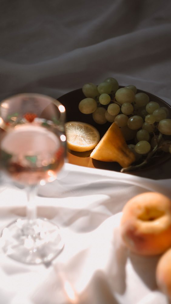 A glass of rose wine arranged with plates of fruit