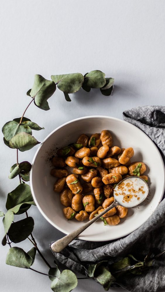 A bowl of gnocchi presented with a branch of leaves and grey linen cloth