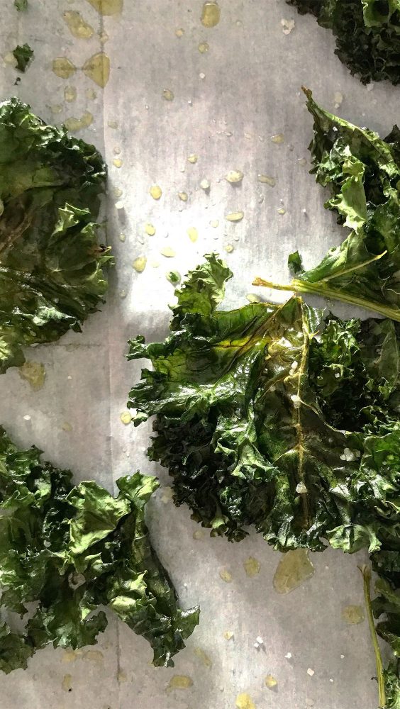 Leaves of kale on a wooden board with sprinkles of salt and oil