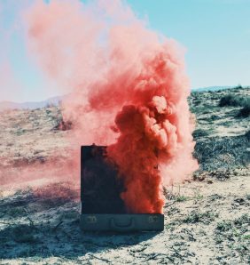 A cloud of pink smoke billows out of a suitcase