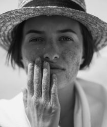 Black and white photograph of model wearing a sun hat holding her face