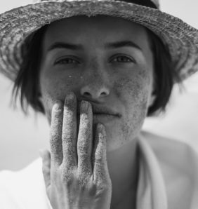 Black and white photograph of model wearing a sun hat holding her face