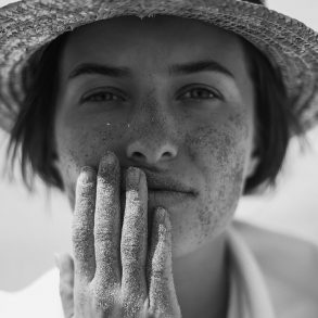 Black and white photograph of model wearing a sun hat holding her face